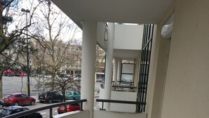 Un balcon carrelé avec une rambarde en métal, donnant sur un parking où sont garées plusieurs voitures.