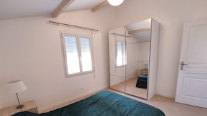 A bedroom with a bed, a wardrobe, a mirror, and a window.