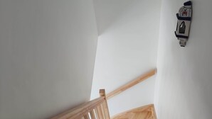 A wooden staircase with a handrail, white walls, and a wall-mounted light fixture.