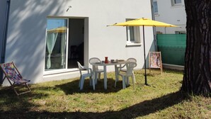 A two-story building with a white exterior, a balcony with a yellow umbrella, and a small table with chairs.