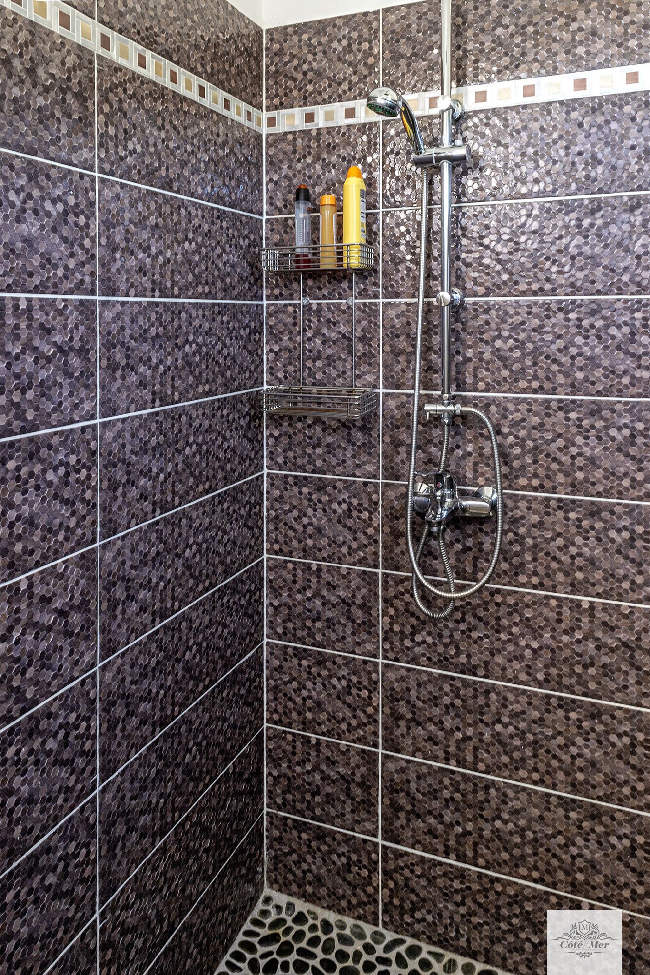 A shower area with a tiled wall, a showerhead, and a soap dispenser on a shelf.