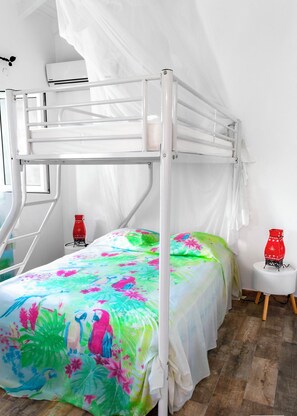 A bunk bed with a colorful floral bedspread, white curtains, and a small bedside table with a red vase.