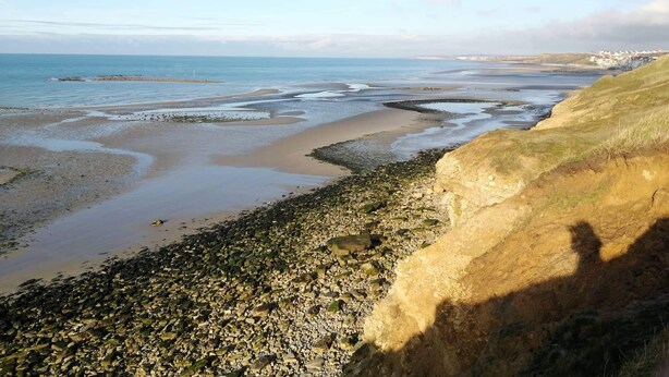 A coastal landscape with a rocky shoreline, a sandy beach, and a distant view of a town. - Welcome to "La Ferme des Tilleuls" (Courset)