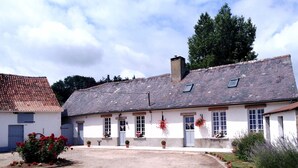 A white building with a tiled roof, multiple windows, and a small garden area with red flowers. - Welcome to "La Ferme des Tilleuls" (Courset)