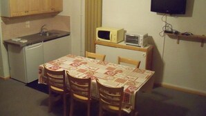 A compact kitchen with a microwave, toaster, and a small refrigerator. There is a dining table with chairs and a television mounted on the wall. - RENT APARTMENT IN THE MOUNTAIN - PIERRA MENTA (Villard-Sur-Doron)