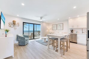 A modern kitchen with white cabinets, a bar area, and a view of the ocean through large sliding doors.