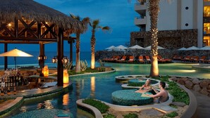 Zona de piscina de un resort con bar, sillas de descanso y una estructura de techo de paja.