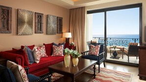 Habitación de hotel con sofá rojo, una mesa de centro de madera y vista al mar desde el balcón.
