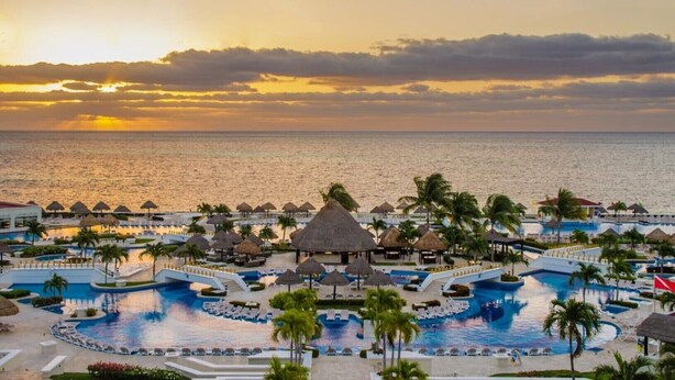 A resort with multiple swimming pools, palm trees, and a view of the ocean at sunset. - Luxury Suite in Moon Palace  Cancún (Cancún)