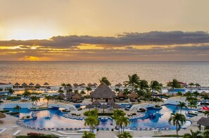 A resort with multiple swimming pools, palm trees, and a view of the ocean at sunset. - Luxury Suite in Moon Palace  Cancún (Cancún)
