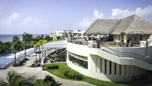 A resort with a pool, outdoor seating, and a thatched-roof building. - Luxury Suite in Moon Palace  Cancún (Cancún)