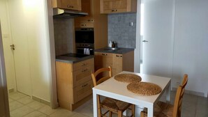 A compact kitchen with wooden cabinets, a built-in oven, and a white dining table with woven placemats.