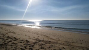 A beach with footprints leading to the water, a clear sky, and the sun shining.