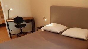 A bedroom with a bed, two pillows, a desk with a chair, and a lamp.