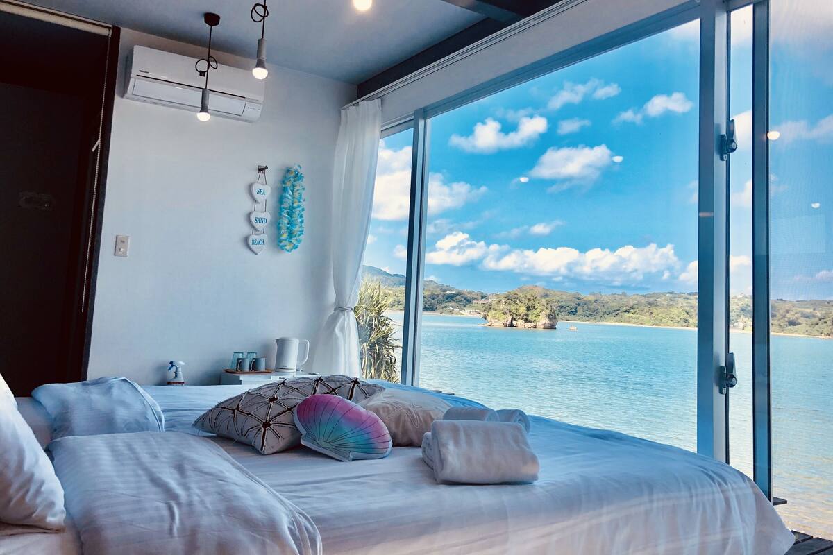 Quarto com uma cama grande, vista para o mar e janela com cortinas.