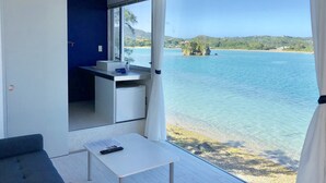 A balcony with a view of a lake, a small table with a remote control, and a kitchenette area. - Nel Beach Rosso & Indigo (Nago)
