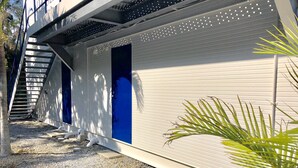 A building with a white exterior, two blue doors, a staircase, and a gravel ground. - Nel Beach Rosso & Indigo (Nago)