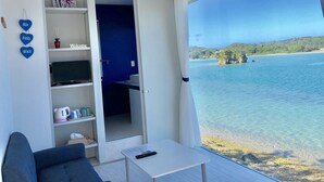 A room with a view of a beach, a sofa, a coffee table, and a shelf with a 'Welcome' sign. - Nel Beach Rosso & Indigo (Nago)