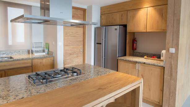 A modern kitchen with granite countertops, stainless steel appliances, wooden cabinets, and a gas stove. - Residence Bel Eau (Mahé Island)
