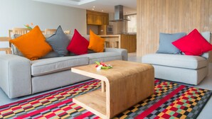 A modern living room with a grey sofa, colorful cushions, a wooden coffee table, and a vibrant patterned rug. - Residence Bel Eau (Mahé Island)