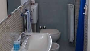 Une petite salle de bain comprenant un lavabo, deux toilettes, une fenêtre et un rideau de douche.
