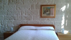 Une chambre à coucher avec un lit en bois, du linge de lit blanc, un mur en briques et un tableau encadré.