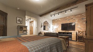 A cozy living room with a large bed, a fireplace, and a television mounted on a brick wall.