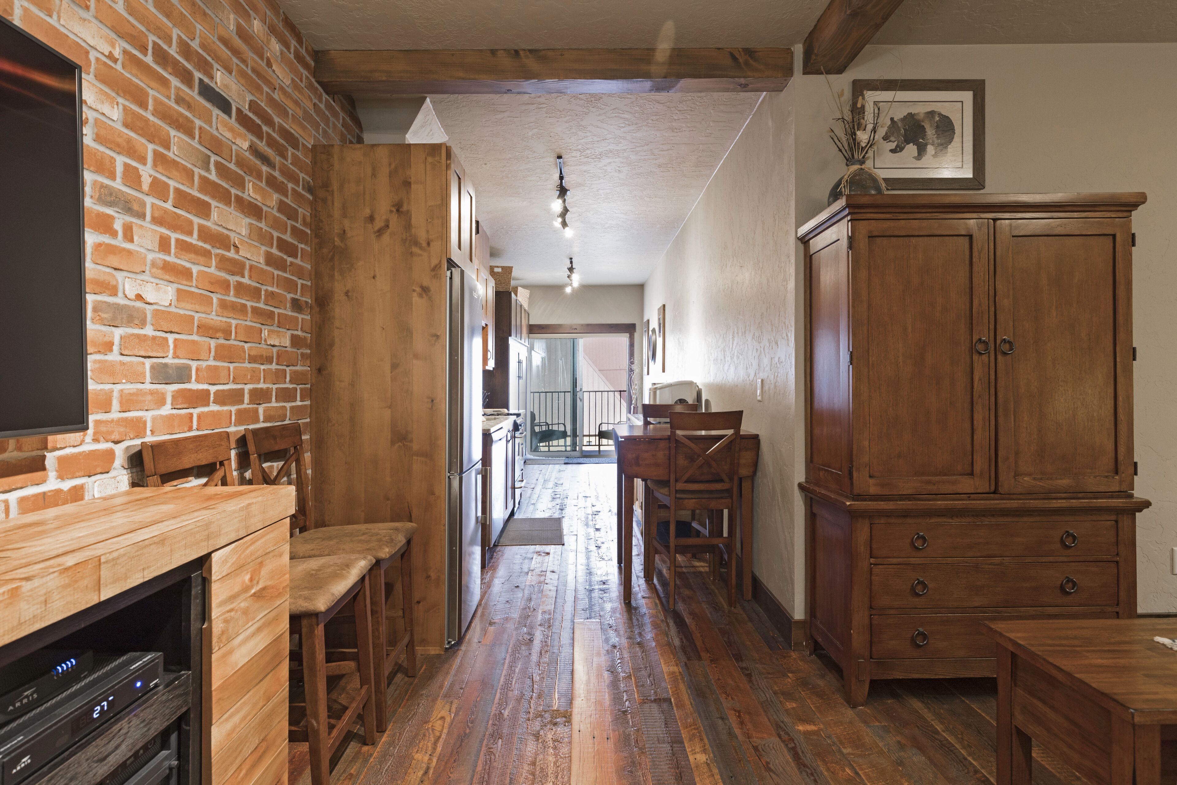 Une cuisine avec un mur en briques, des meubles en bois et un coin repas comprenant des chaises et une table.
