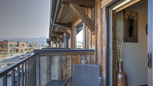 A balcony with a metal chair, a vase with plants, and a view of a street and mountains.