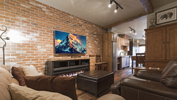 A cozy living room with a brick wall, a fireplace, leather sofas, and a flat-screen TV.