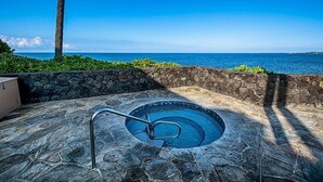 Una piscina de piedra con una escalera de metal, rodeada por un muro de piedra y vegetación, con vistas al océano azul y despejado.