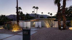 Ein modernes Haus mit minimalistischem Design, umgeben von einer Schotterauffahrt und Palmen.