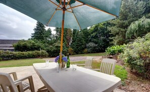 Eine Terrasse im Freien mit Tisch, Stühlen, einem großen Sonnenschirm und einer Weinflasche.