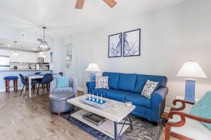 Uma sala de estar moderna com um sofá azul, uma mesa de centro e um espaço de jantar com cadeiras e uma mesa.