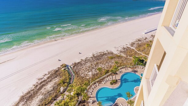 A beach view with a pool and a pier in the distance.