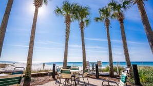 A beachside patio with palm trees, outdoor seating, and a view of the ocean.