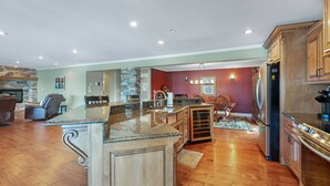 A spacious kitchen with a large island, wooden cabinets, and a stone fireplace. - Giant Lakefront Home with spectacular views of main channel - Lake of the Ozarks (Osage Beach)