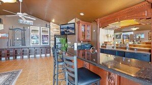 A bar area with a counter, stools, a television, and a ceiling fan. - Giant Lakefront Home with spectacular views of main channel - Lake of the Ozarks (Osage Beach)