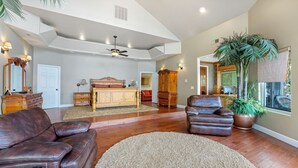 A spacious living room with a large wooden bed, leather sofas, a dining area, and a view of the outdoors. - Giant Lakefront Home with spectacular views of main channel - Lake of the Ozarks (Osage Beach)