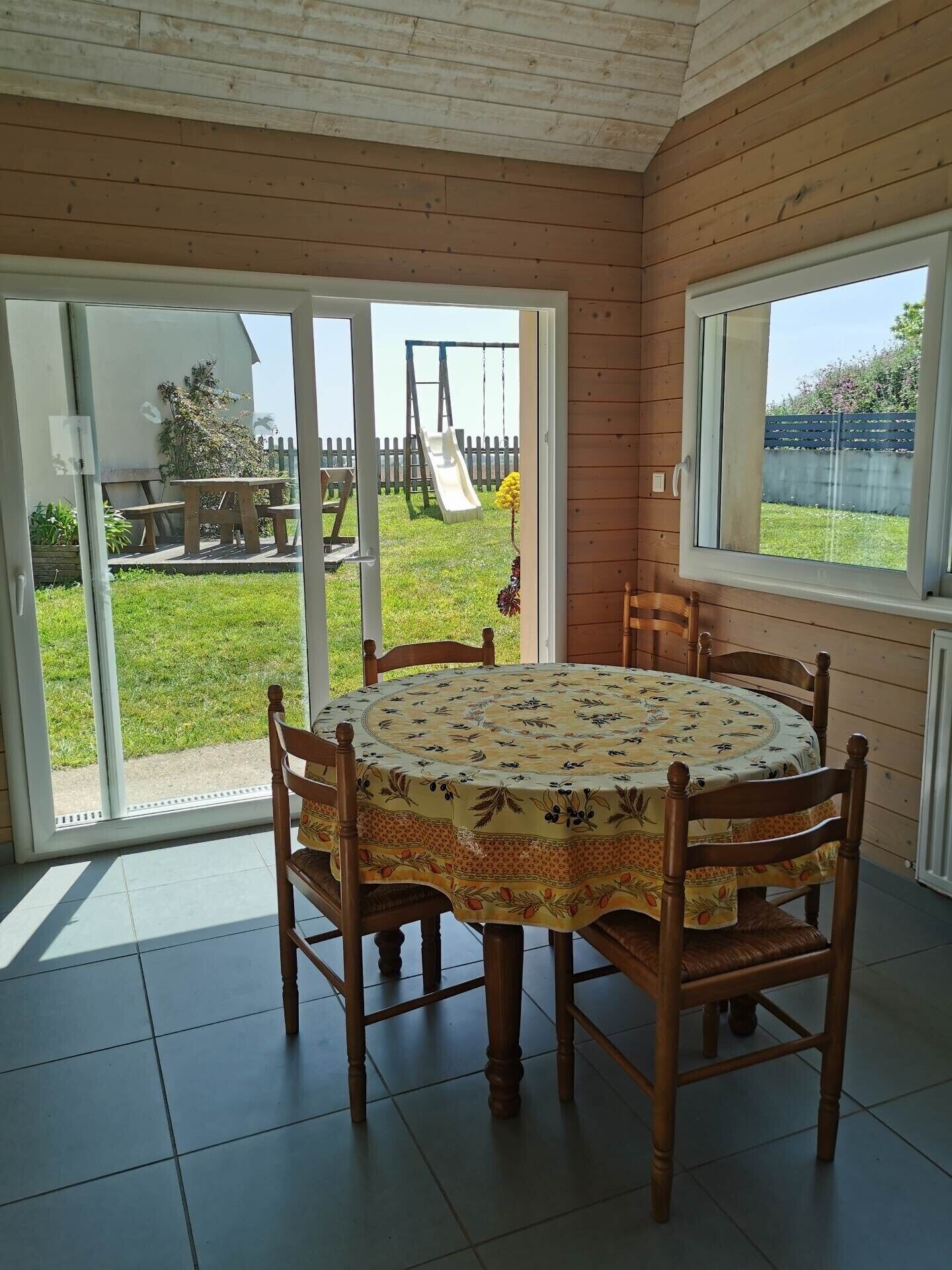 A dining area with a round table covered by a floral tablecloth, surrounded by wooden chairs.