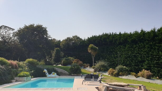 A rectangular swimming pool with a tiled deck, surrounded by a grassy area and various plants. - Gîte de Penn Ar Roz: 3 épis seaside GUILER-SUR-GOYEN, 4-5 pers, swimming pool. (Guiler-sur-Goyen)