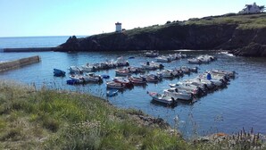 A harbor with numerous small boats docked in calm waters, surrounded by grassy cliffs and a lighthouse in the background. - Gîte de Penn Ar Roz: 3 épis seaside GUILER-SUR-GOYEN, 4-5 pers, swimming pool. (Guiler-sur-Goyen)