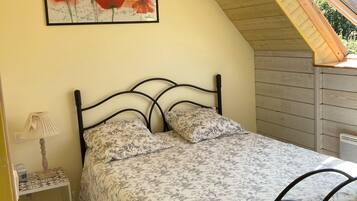 Une chambre avec un plafond en pente, un lit recouvert d’une couvre-lit à motifs floraux, une table de chevet avec une lampe et un tableau encadré accroché au mur.