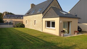 A stone house with a sloped roof, a small attached garage, and a well-maintained lawn. - Gîte de Penn Ar Roz: 3 épis seaside GUILER-SUR-GOYEN, 4-5 pers, swimming pool. (Guiler-sur-Goyen)