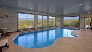An indoor swimming pool with large windows offering a view of the surrounding landscape.