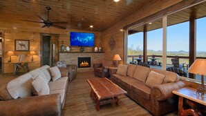A cozy cabin interior with a fireplace, wooden furniture, and a large window offering a view of the mountains.