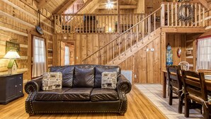 Ein Interieur einer Holzhütte mit Ledersofa, Esstisch und Treppe.