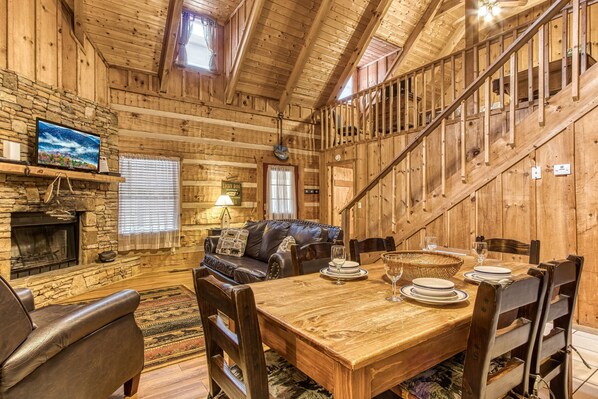 Cozy cabin-style retreat with a stone fireplace, leather sofa, and wooden dining table.