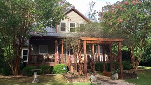 A two-story house with a porch, surrounded by lush greenery and flowering trees. - 3+ acres of woods and lake (Bremen)