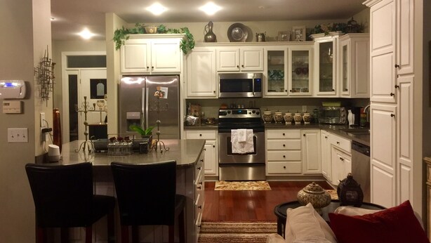 A modern kitchen with white cabinets, stainless steel appliances, and a central island with chairs. - 3+ acres of woods and lake (Bremen)